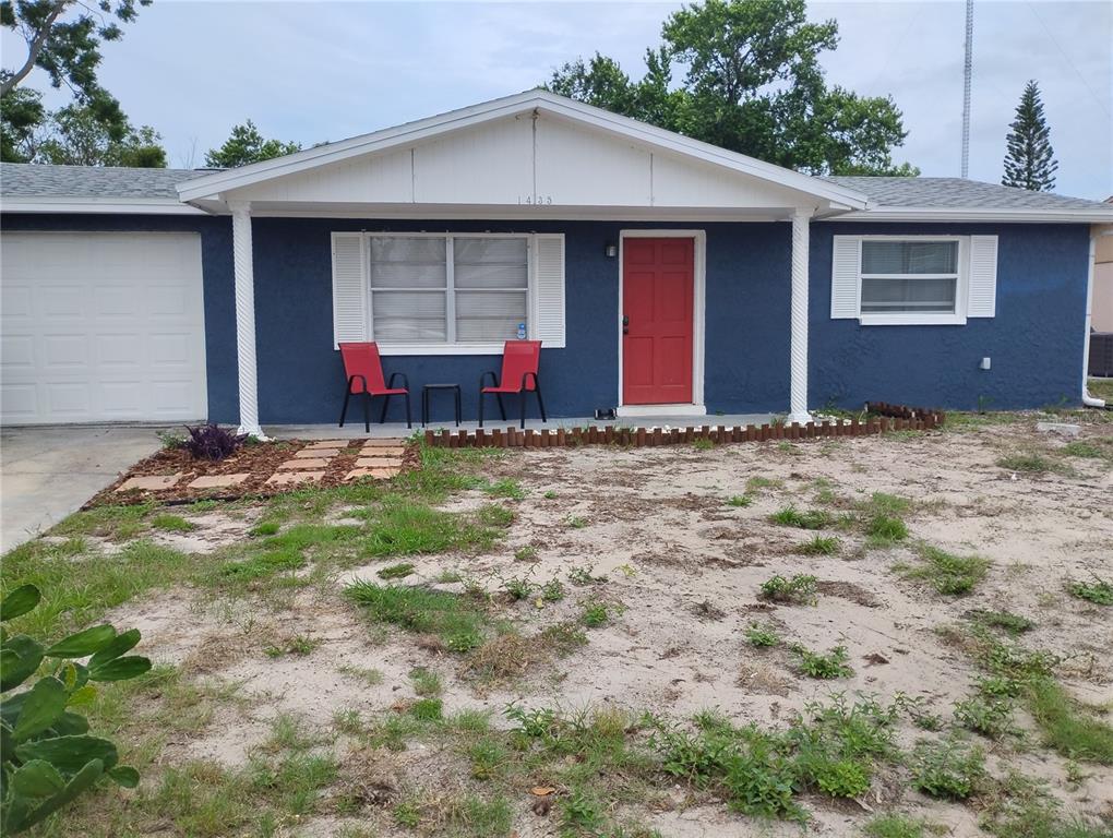 A blue single-story house features a red front door, white trim, and a sandy yard — 1435 WHITEHALL LANE, HOLIDAY, FL