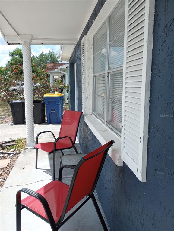 A covered porch features two red chairs, a small table, and a blue exterior wall — 1435 WHITEHALL LANE, HOLIDAY, FL