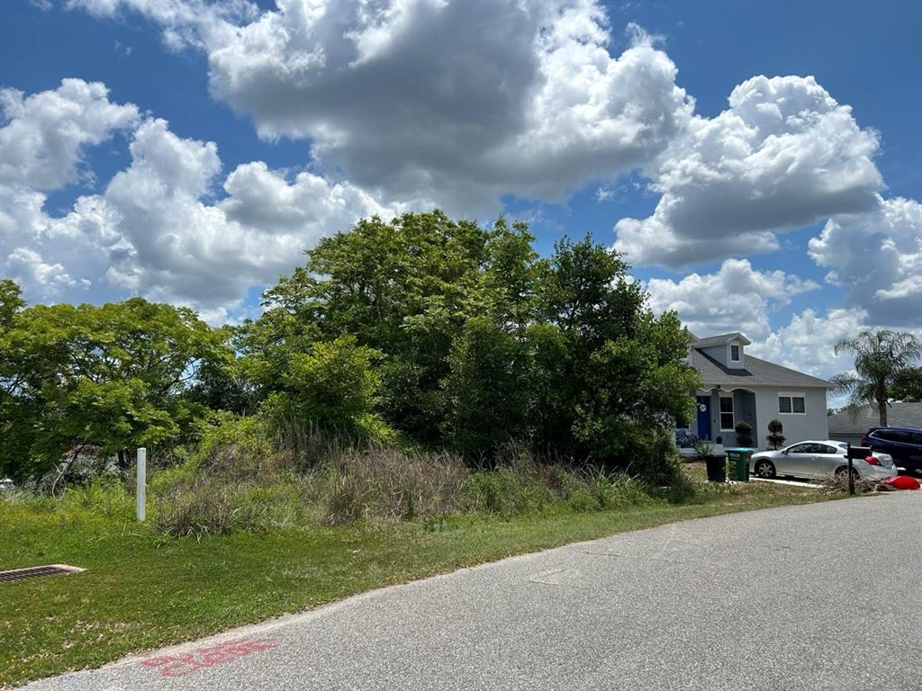 A vacant, overgrown lot sits next to a single-story house under a cloudy blue sky — 2055 E PRAIRIE CIR #50, DELTONA, FL