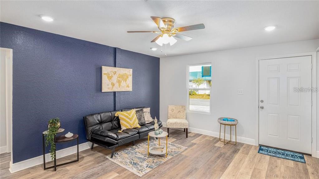 A living room features a dark blue accent wall, a black sofa, and wood-look flooring — 7508 CAROLYN AVENUE, ORLANDO, FL