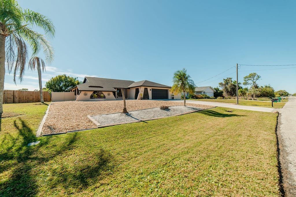 A single-story house with a gravel front yard, palm trees, and a dark garage door — 9273 CARNATION AVENUE, ENGLEWOOD, FL