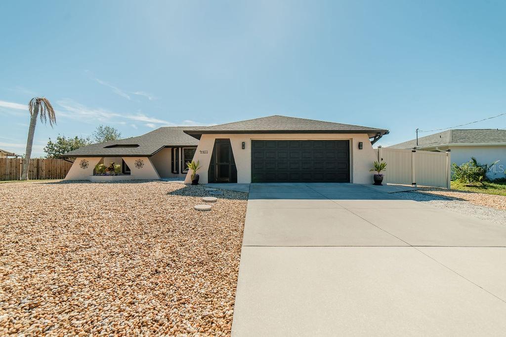 A single-story house with a beige exterior, a dark garage door, and a gravel front yard — 9273 CARNATION AVENUE, ENGLEWOOD, FL