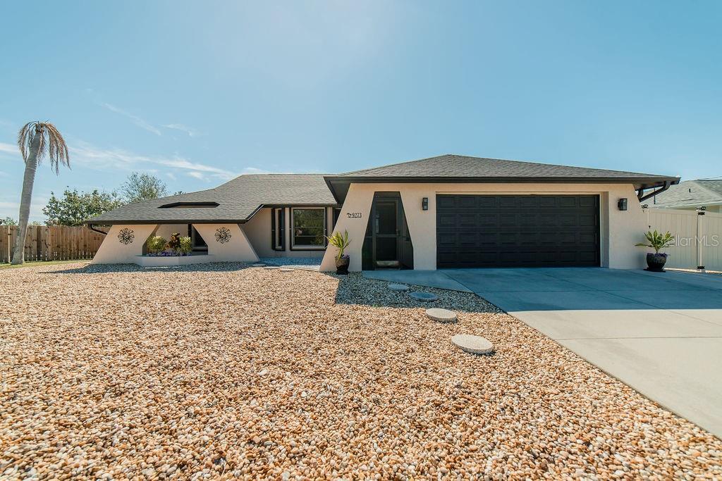 A single-story house with a beige stucco exterior, dark roof, and a gravel front yard — 9273 CARNATION AVENUE, ENGLEWOOD, FL