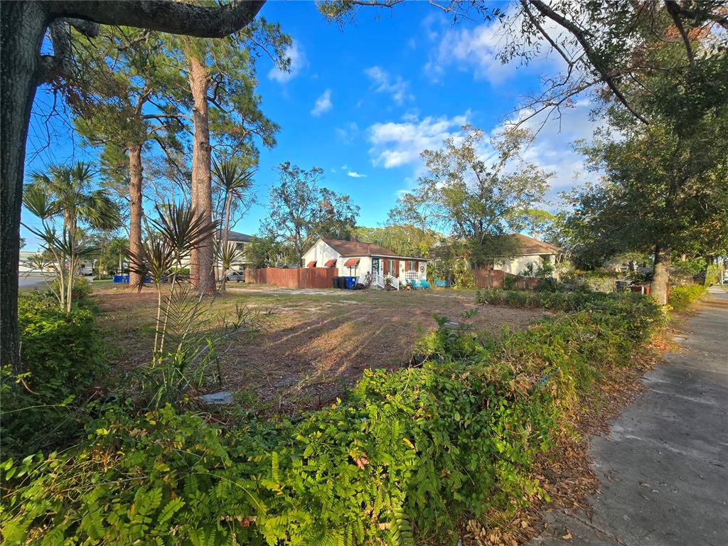 A vacant lot with sparse vegetation sits in front of a small house and trees — 237 50TH AVENUE N, ST PETERSBURG, FL