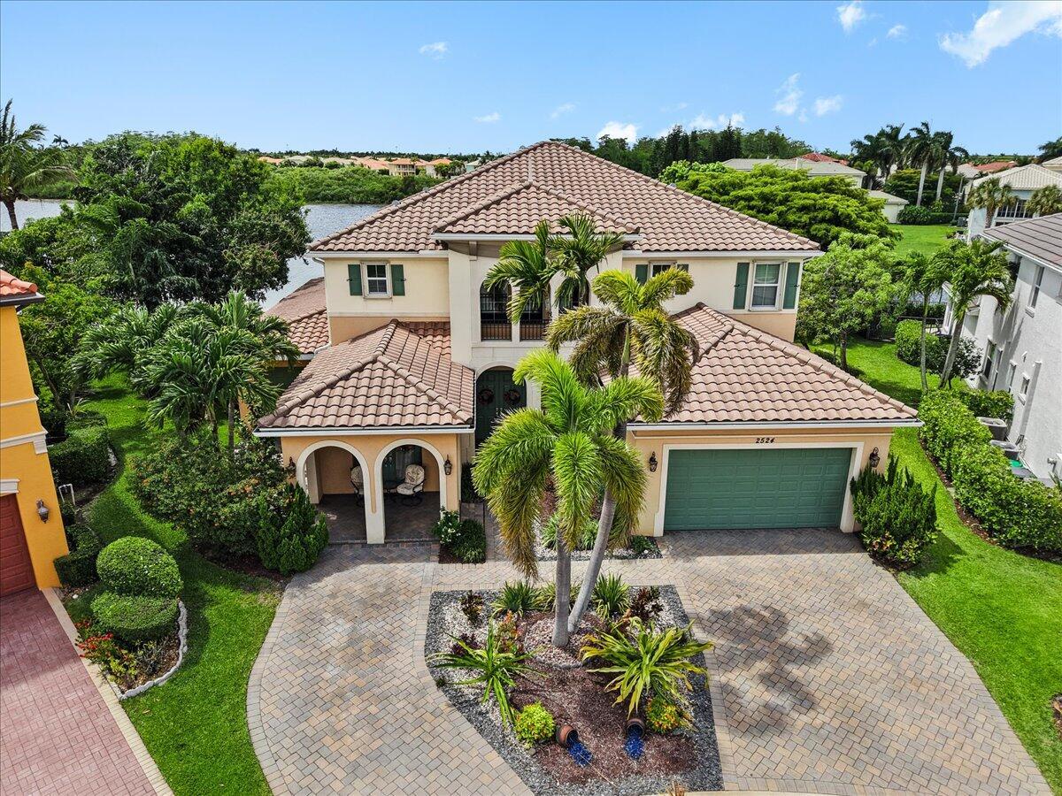 A covered patio features two patterned chairs, a small table, and green French doors — 2524 Cooper Way, Wellington FL 33414, WELLINGTON, FL