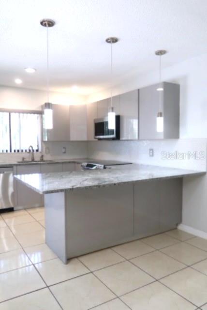 A modern kitchen features gray cabinets, stainless steel appliances, a marble island, and bar stools — 15202 E POND WOODS DRIVE UNIT 9, TAMPA, FL