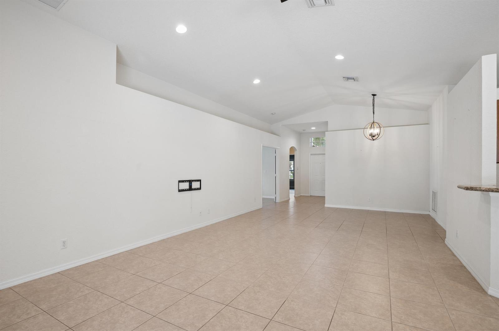 An empty living room features vaulted ceilings, tile flooring, and a wall-mounted television bracket — 5330 Vernio Lane, Boynton Beach FL 33437, BOYNTON BEACH, FL
