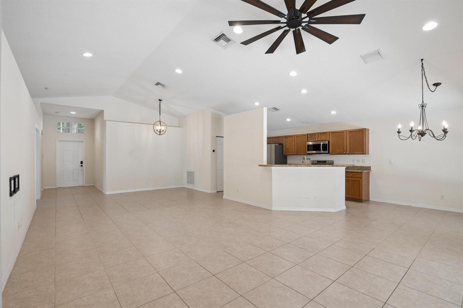 An open-concept living and dining area features tile flooring, a kitchen with wood cabinets, and vaulted ceilings — 5330 Vernio Lane, Boynton Beach FL 33437, BOYNTON BEACH, FL