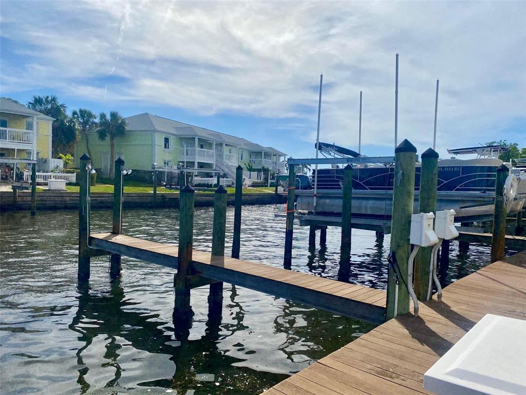 A wooden dock extends into a canal toward a pontoon boat and waterfront homes — 0 NE BEACH DRIVE SE UNIT 95SS, ST PETERSBURG, FL