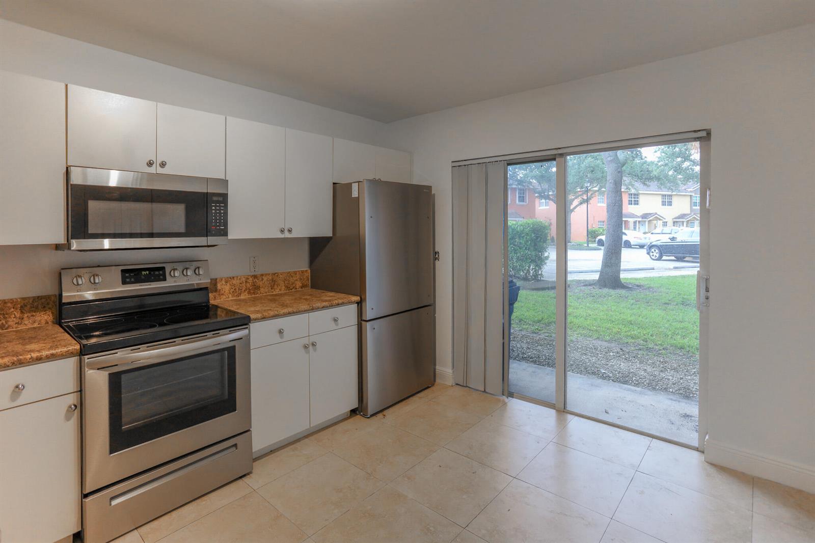 A kitchen with white cabinets, stainless steel appliances, tan countertops, and a sliding glass door — 4149 NW 67th Te # 4149, Lauderhill FL 33319, LAUDERHILL, FL