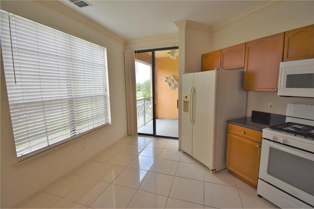 An open-concept kitchen with wood cabinets and a breakfast bar overlooks a living area — 2722 VIA TIVOLI UNIT 420A, CLEARWATER, FL