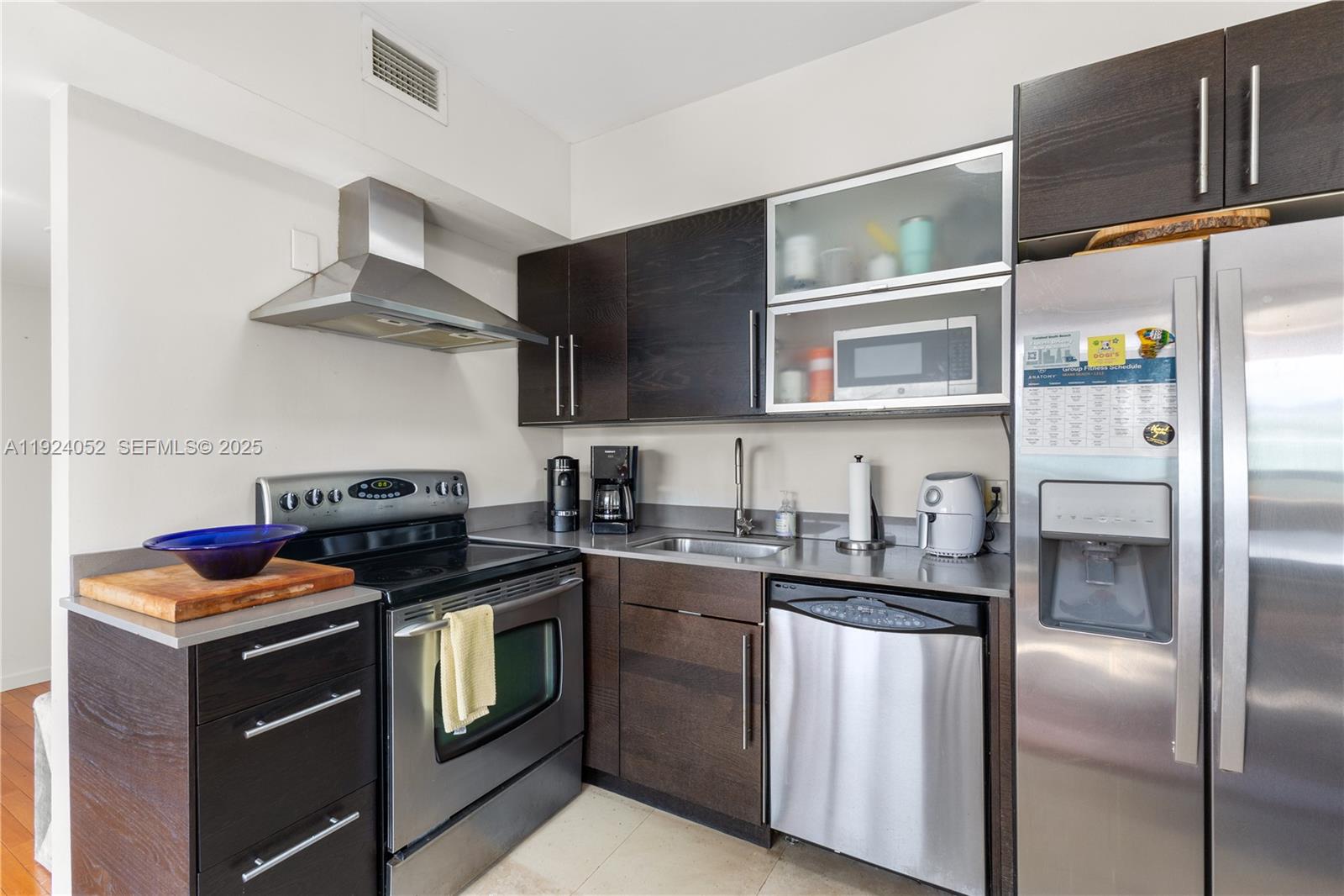A compact kitchen features dark wood cabinets, stainless steel appliances, and a small sink — 1330 West Ave # 1712, Miami Beach FL 33139, MIAMI BEACH, FL