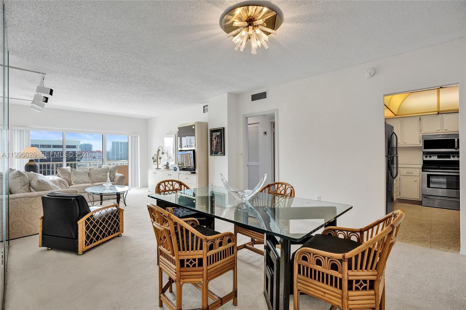 A dining area with a glass table and rattan chairs opens into a living room — 1985 S Ocean Dr # 12A, Hallandale Beach FL 33009, HALLANDALE BEACH, FL