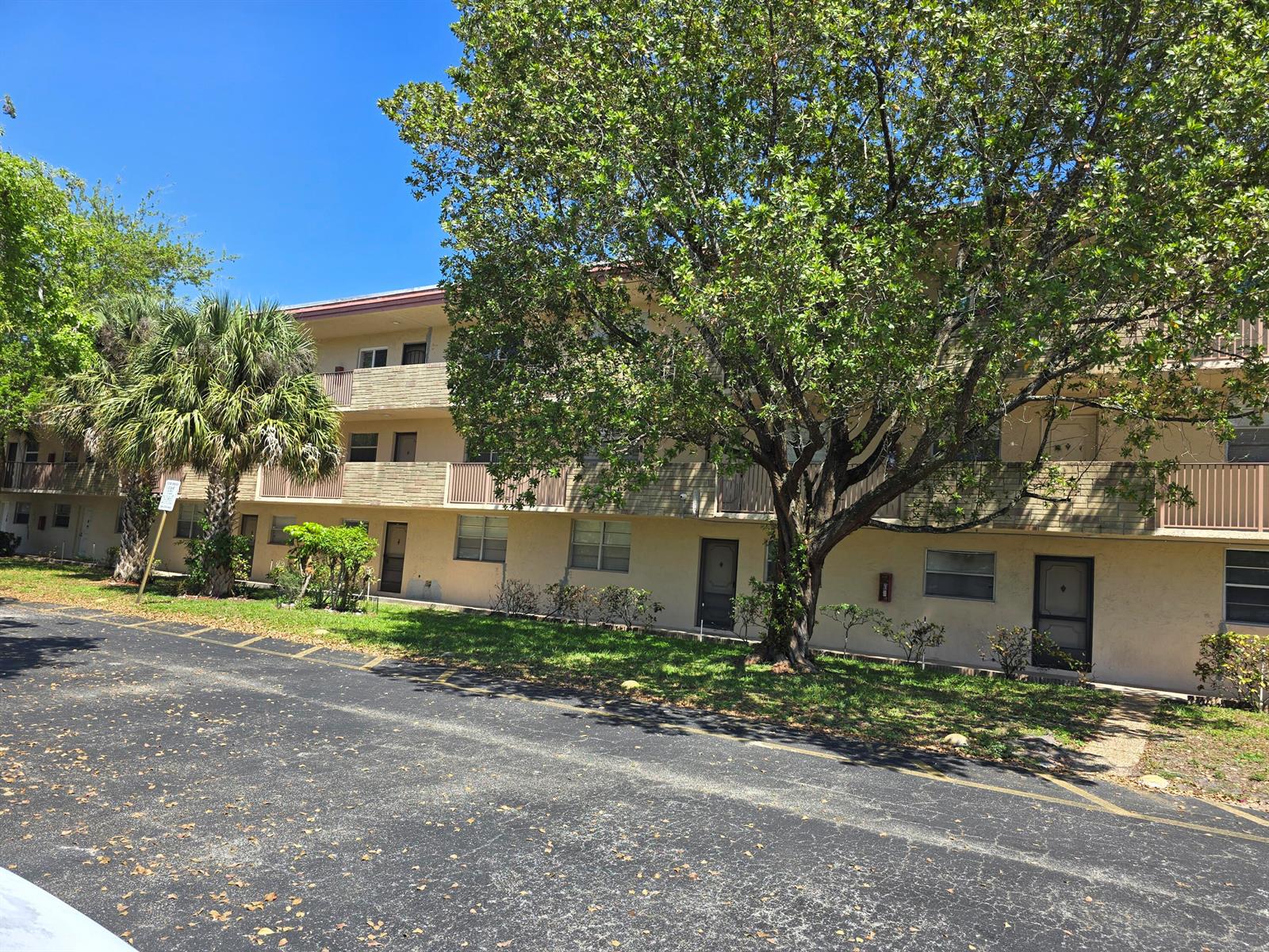 A three-story apartment building with beige siding, balconies, and a large tree in front — 3900 NW 76th Avenue # 107, Sunrise FL 33351, SUNRISE, FL