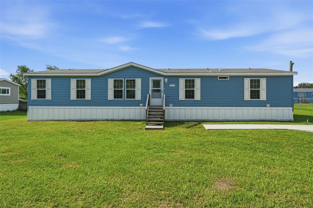 A blue manufactured home with white trim sits on a grassy lot under a blue sky — 6161 SE 145TH STREET, SUMMERFIELD, FL