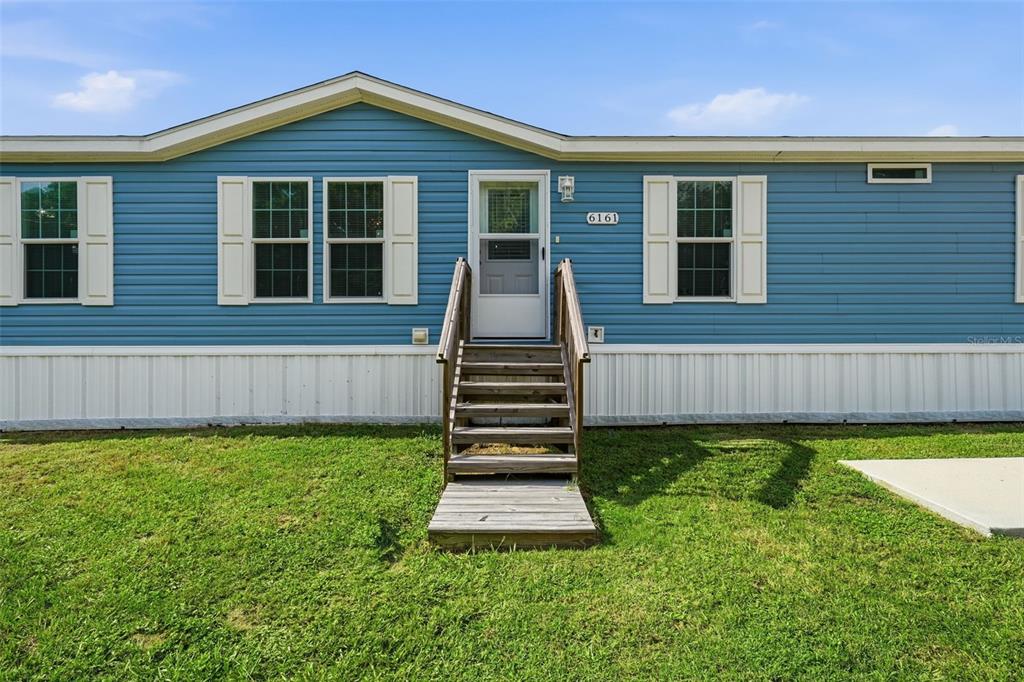 A blue-sided manufactured home features a central wooden staircase leading to the front door — 6161 SE 145TH STREET, SUMMERFIELD, FL
