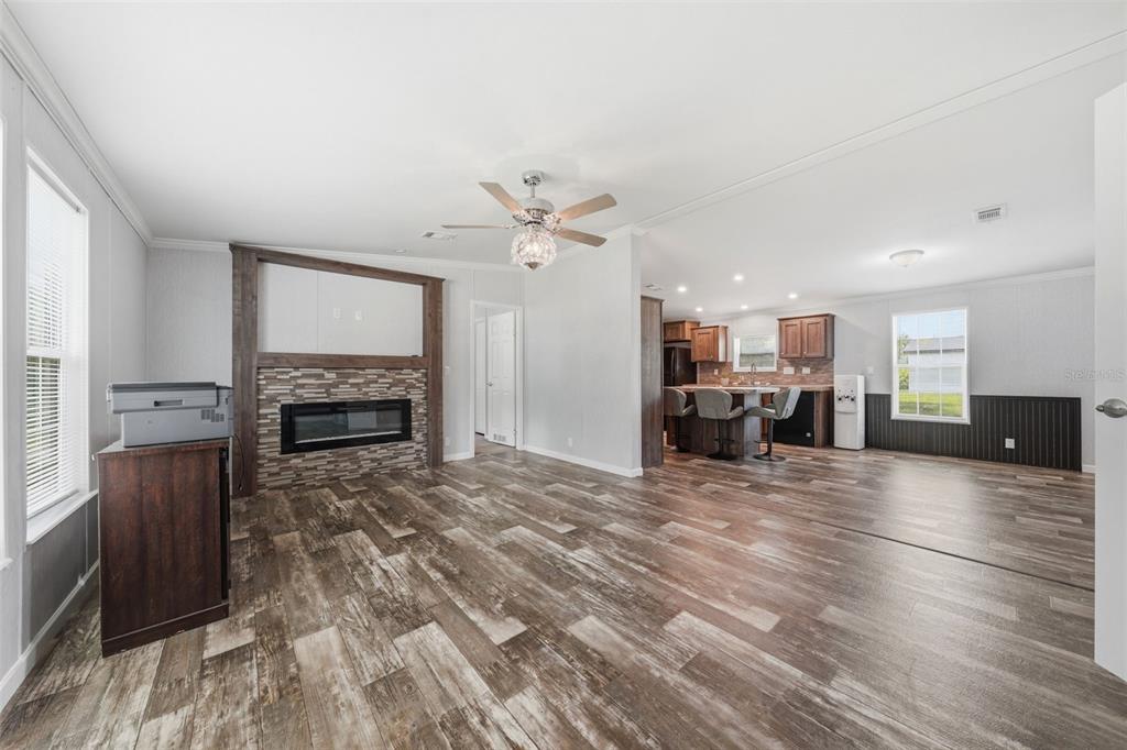An open-concept living room and kitchen featuring wood-look flooring, a stone fireplace, and wood cabinetry — 6161 SE 145TH STREET, SUMMERFIELD, FL