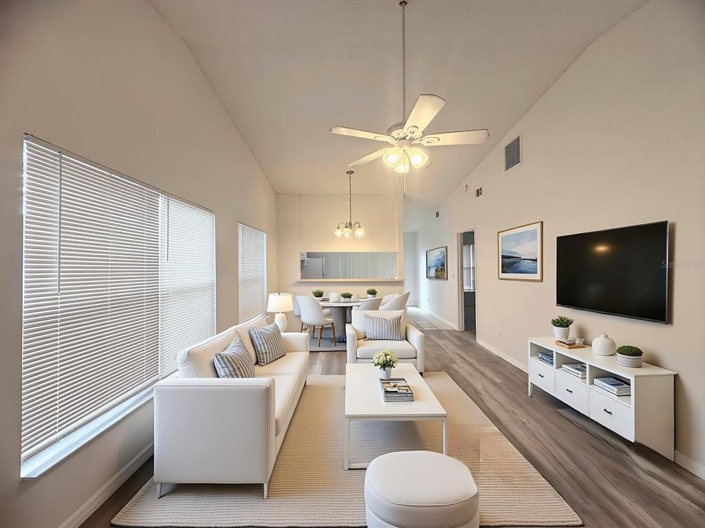 A bright living and dining area features white furniture, wood-look flooring, and a vaulted ceiling — 1947 BENTLEY BOULEVARD, KISSIMMEE, FL