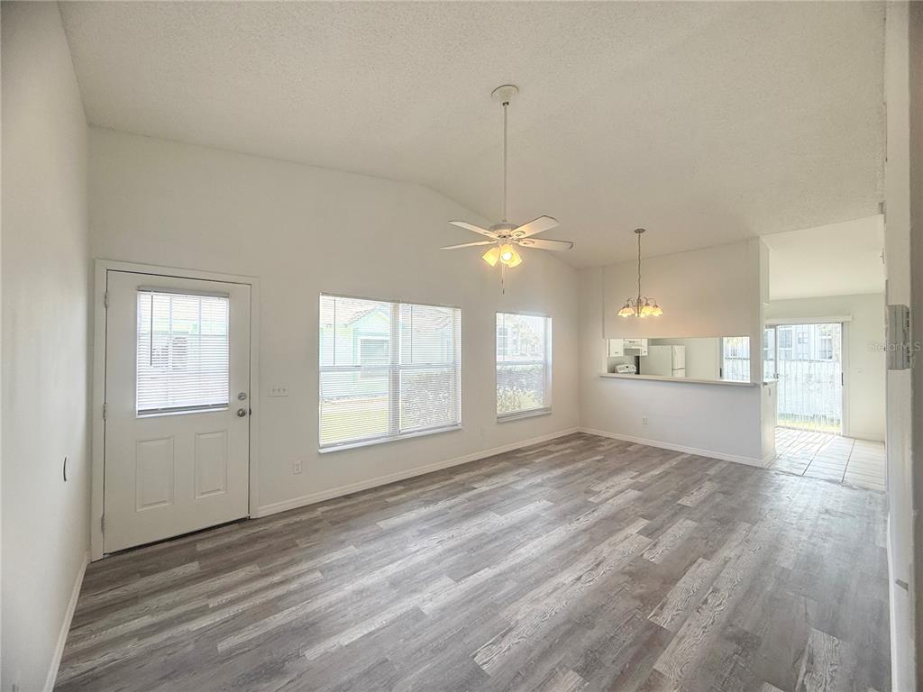 An empty living room with wood-look flooring, a ceiling fan, and a pass-through kitchen window — 1947 BENTLEY BOULEVARD, KISSIMMEE, FL