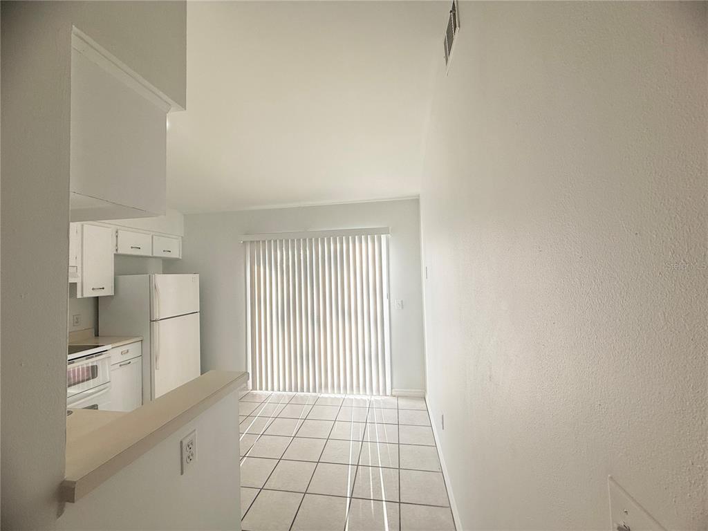 A kitchen with white cabinets and appliances opens to a tiled dining area with blinds — 1947 BENTLEY BOULEVARD, KISSIMMEE, FL