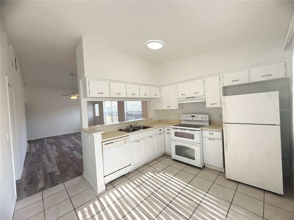A kitchen with white cabinets, white appliances, and tiled flooring opens to a living area — 1947 BENTLEY BOULEVARD, KISSIMMEE, FL
