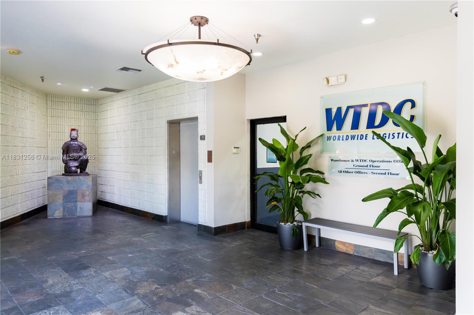A lobby features a stone statue, an elevator, a glass sign, and two large potted plants — 2801 NW 74 AV # S15, Miami FL 33122, MIAMI, FL