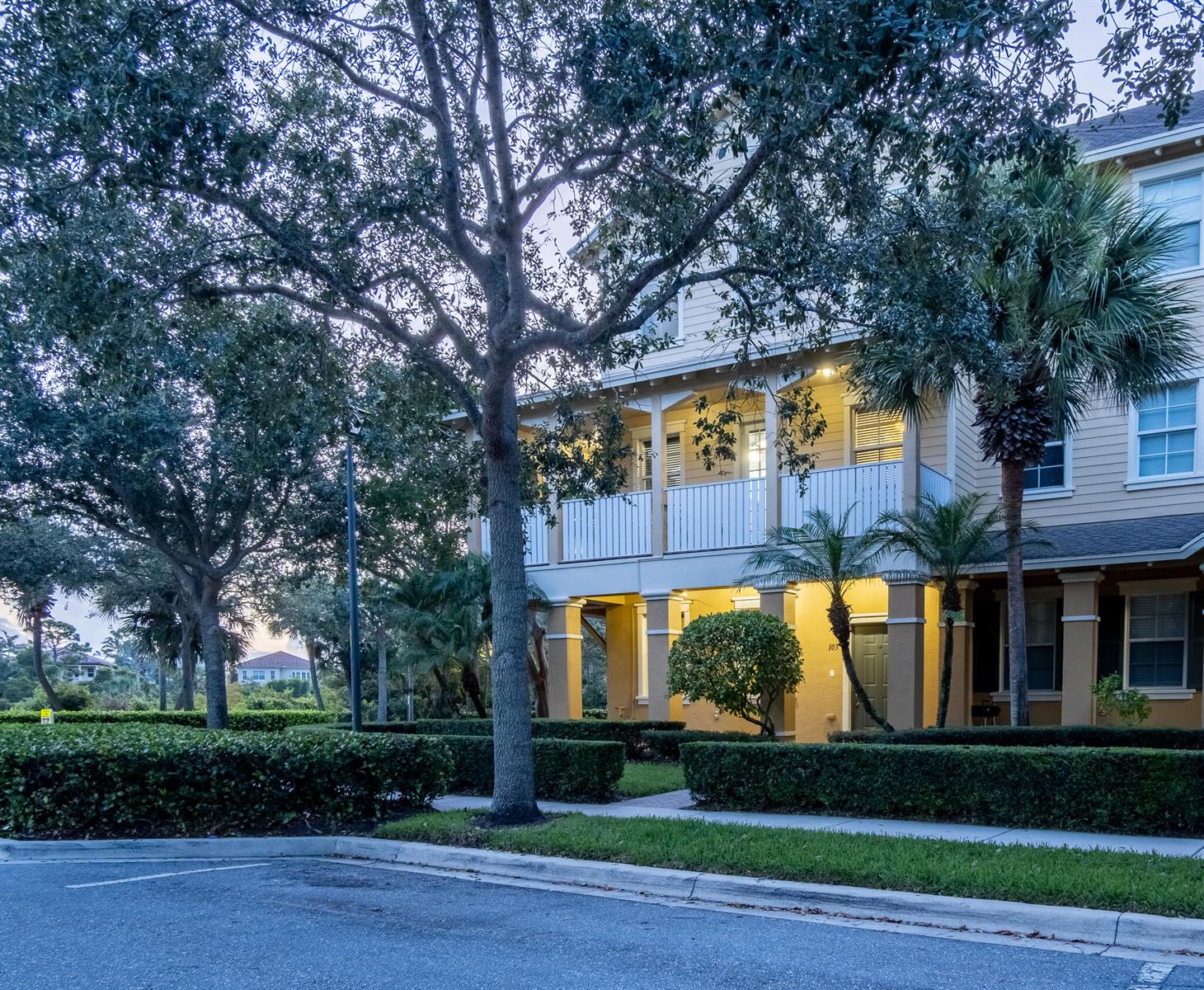A multi-story tan building with a covered porch, balcony, and manicured hedges at dusk — 103 E Thatch Palm Circle, Jupiter FL 33458, JUPITER, FL