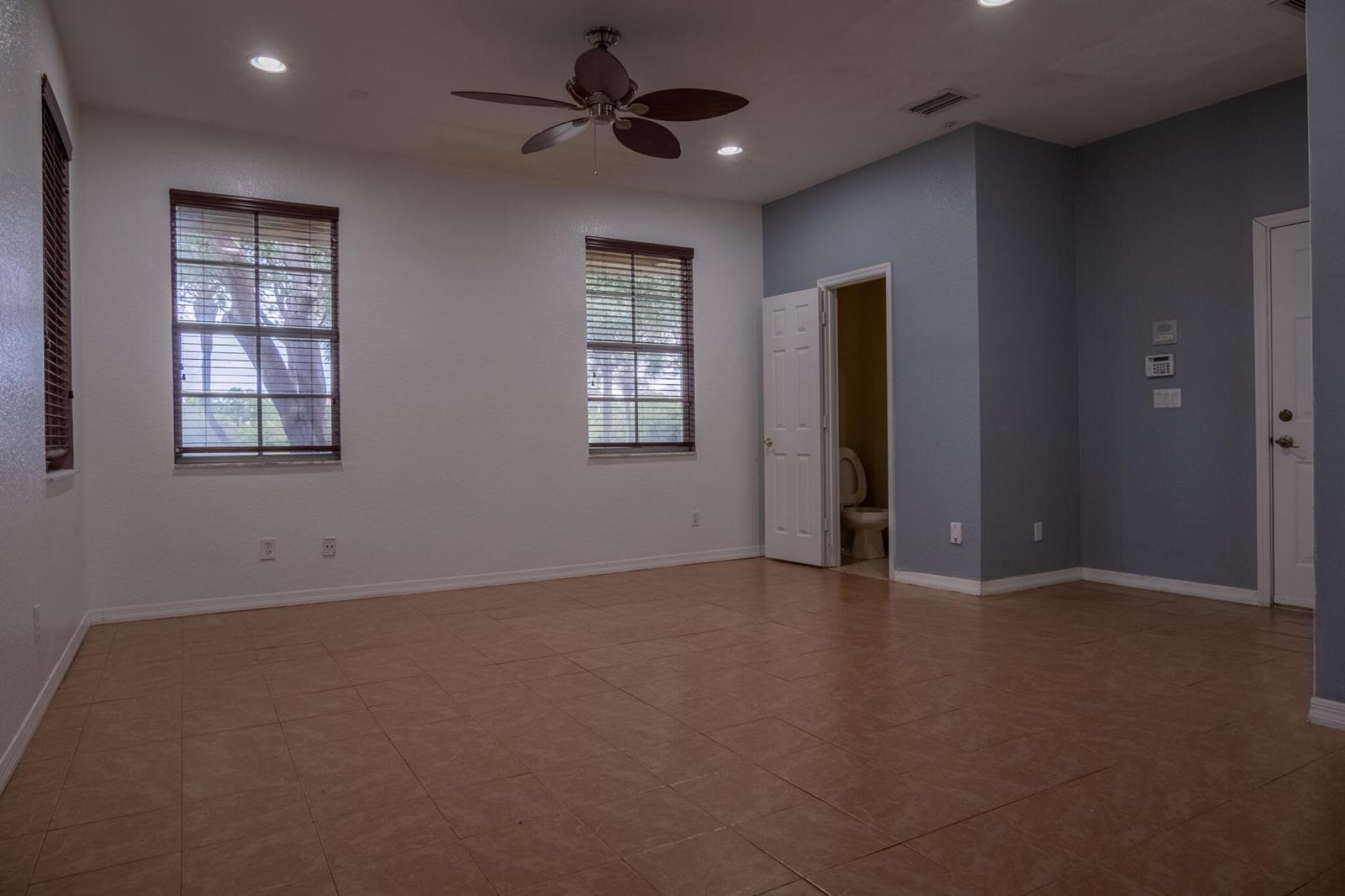 An empty room with tile flooring, two windows with blinds, a ceiling fan, and blue accents — 103 E Thatch Palm Circle, Jupiter FL 33458, JUPITER, FL