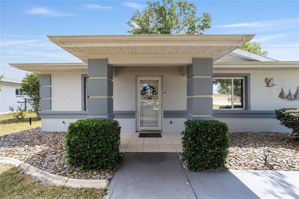 The exterior of a single-story house features a covered entryway with gray columns and landscaping — 10169 SW 63RD AVENUE, OCALA, FL