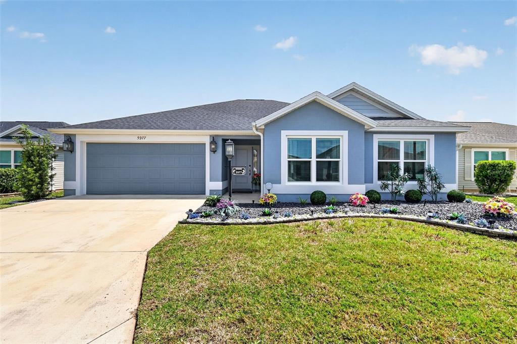 A single-story house with a blue exterior, a two-car garage, and a landscaped front yard — 5977 PHEIL PATH, THE VILLAGES, FL