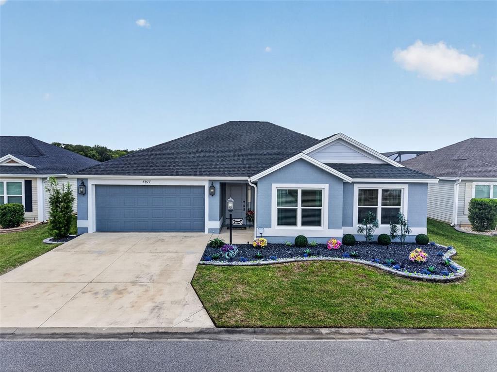 A single-story house with a blue exterior, a two-car garage, and a landscaped front yard — 5977 PHEIL PATH, THE VILLAGES, FL