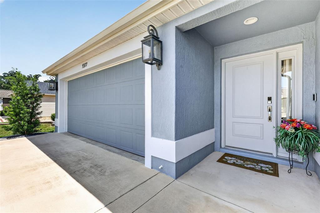 A blue house exterior features a garage, a white front door, and a small potted plant — 5977 PHEIL PATH, THE VILLAGES, FL