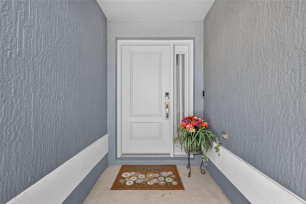 A white front door with a side window sits between two gray textured walls — 5977 PHEIL PATH, THE VILLAGES, FL