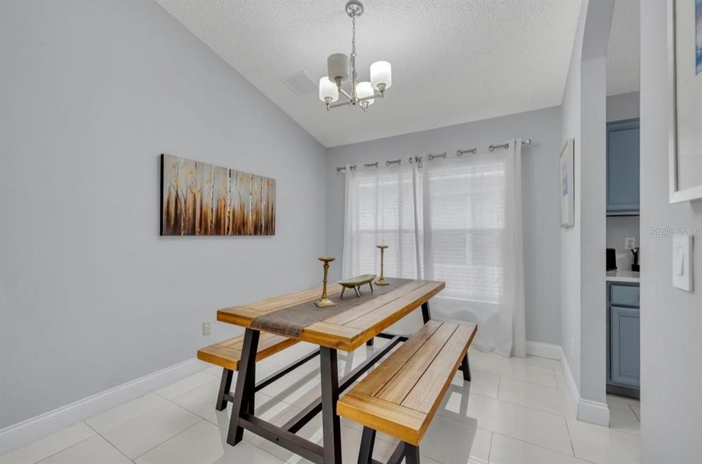 A dining room features a wooden table with two benches, a chandelier, and light walls — 134 MADIERA BEACH BOULEVARD, KISSIMMEE, FL