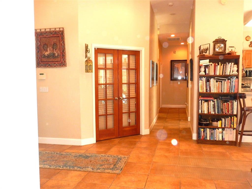A tiled hallway features a wooden bookshelf, French doors, and a decorative wall tapestry — 8315 LILLY LAKE ROAD, MELROSE, FL