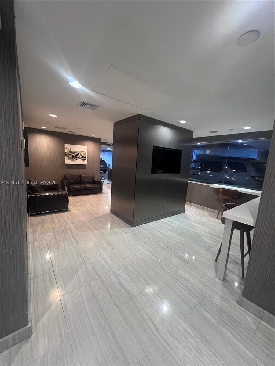 A modern lounge area features a central dark partition with a television and tiled flooring — 150 SE 2nd Ave # 208, Miami FL 33131, MIAMI, FL