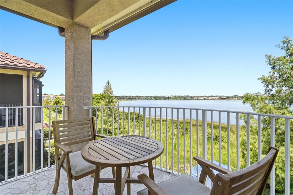A balcony with a wooden table and chairs overlooks a lake and grassy landscape — 8737 THE ESPLANADE UNIT 64, ORLANDO, FL