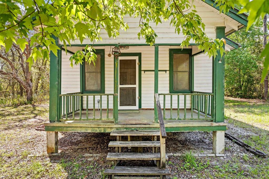 A small white house with a green-trimmed front porch and wooden stairs — 11317 SALINA STREET, BROOKSVILLE, FL