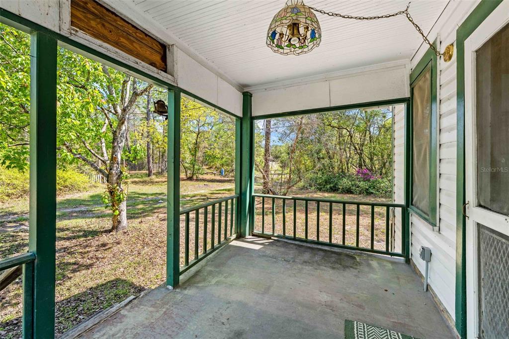 A covered porch with a concrete floor, green railings, and a stained-glass pendant light — 11317 SALINA STREET, BROOKSVILLE, FL