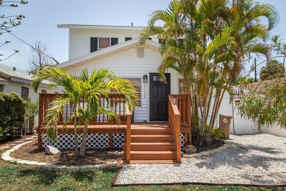 A white two-story house features a wooden front deck, stairs, and palm trees — 13148 3RD STREET E, ST PETERSBURG, FL