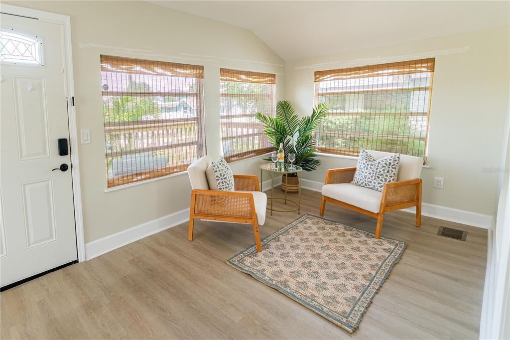 A bright sunroom features light wood flooring, two rattan chairs, a small table, and windows — 13148 3RD STREET E, ST PETERSBURG, FL