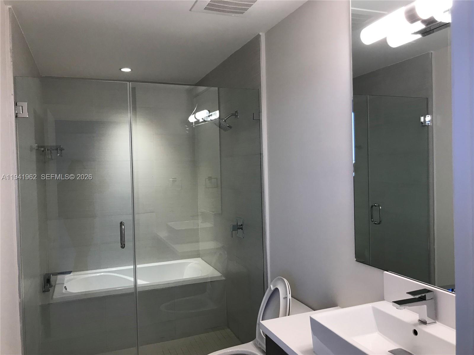A modern bathroom features a glass-enclosed tub and shower combination, a vanity, and a toilet — 1010 SW 2nd Ave # 506, Miami FL 33130, MIAMI, FL