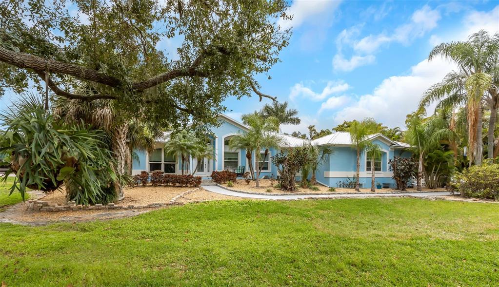 A light blue single-story house with a metal roof is surrounded by lush tropical landscaping — 424 ISLAND CAY WAY, APOLLO BEACH, FL