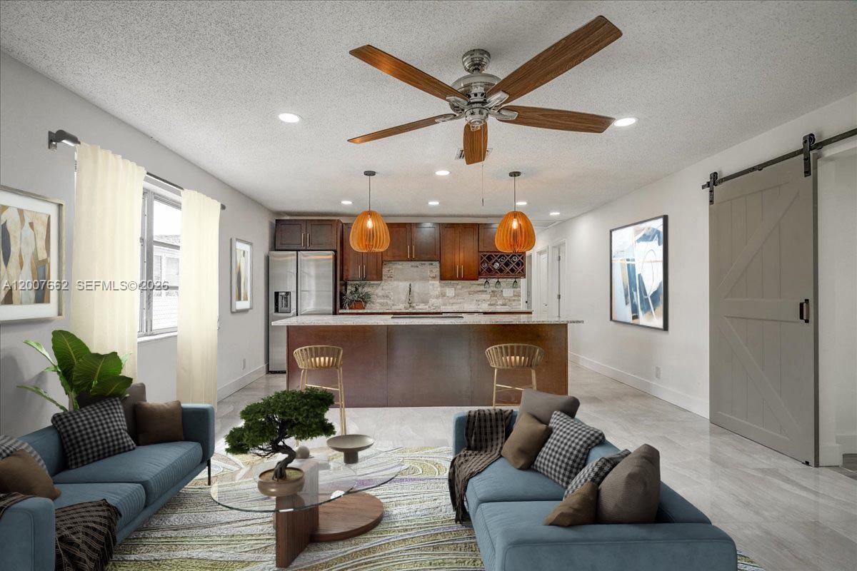 This open-concept living room and kitchen features blue sofas, a wooden island, and wood-toned cabinetry — 1480 W 36th St, Riviera Beach FL 33404, RIVIERA BEACH, FL