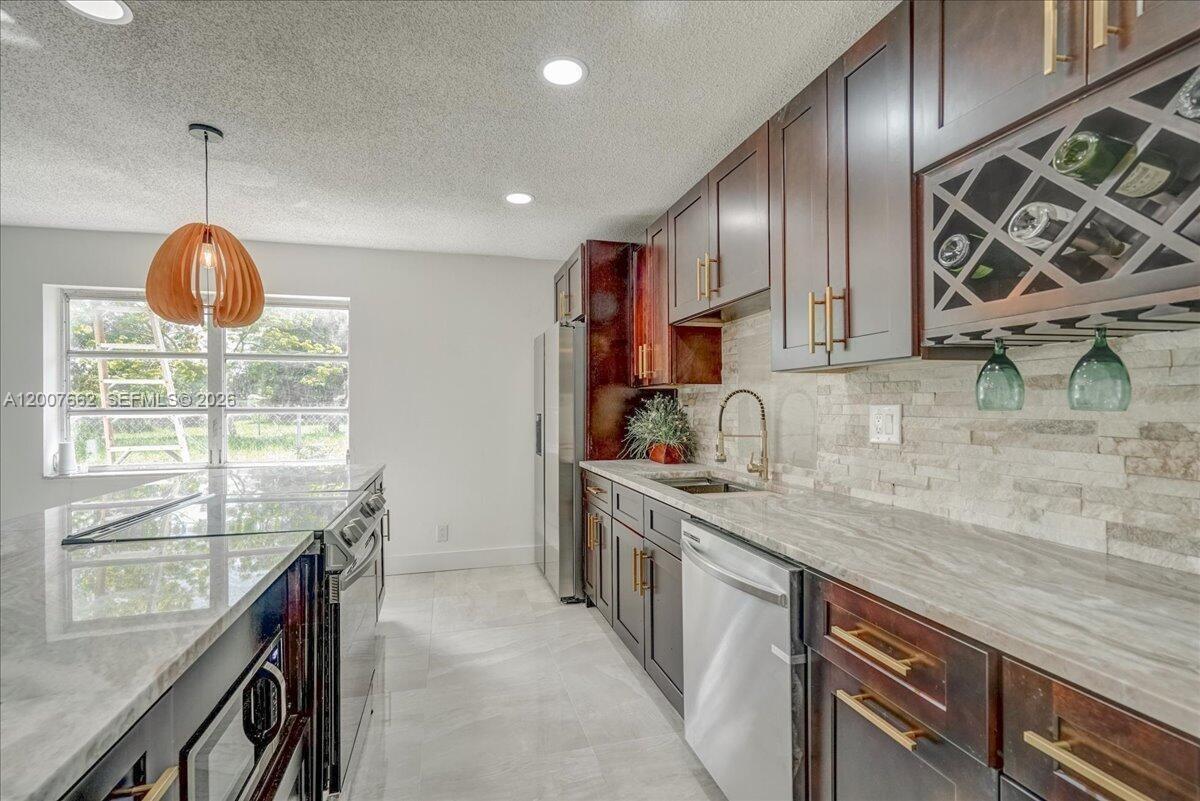 A modern kitchen features dark wood cabinets, stone countertops, and a glass-topped island — 1480 W 36th St, Riviera Beach FL 33404, RIVIERA BEACH, FL