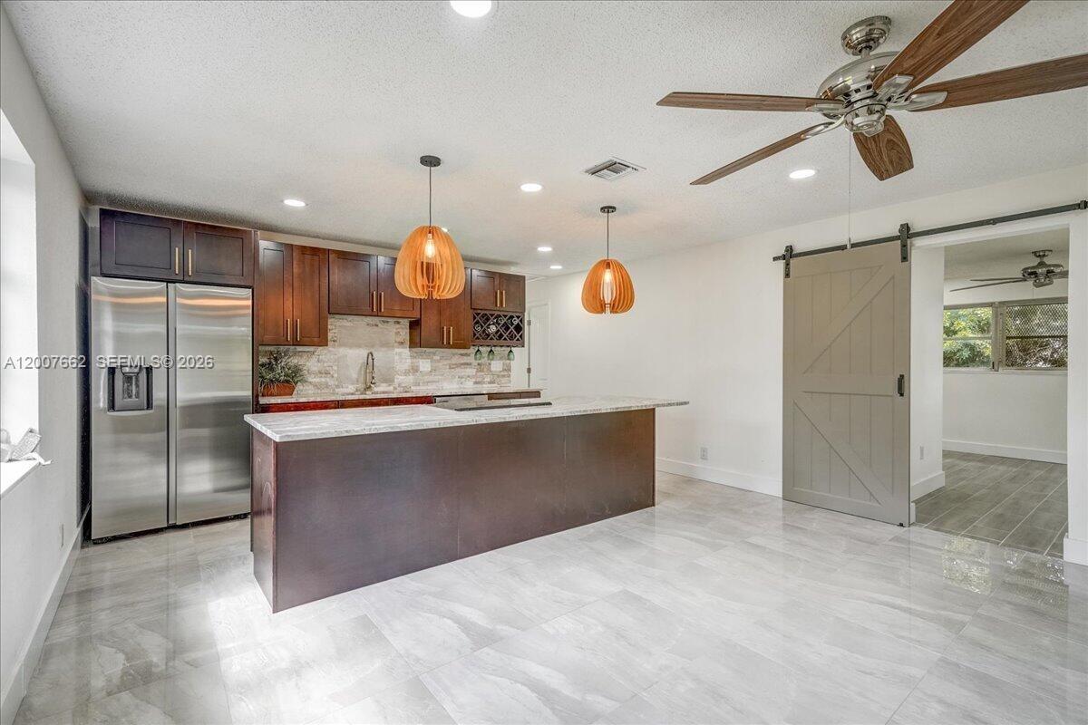 A kitchen features dark wood cabinets, a stone island, and a gray sliding barn door — 1480 W 36th St, Riviera Beach FL 33404, RIVIERA BEACH, FL