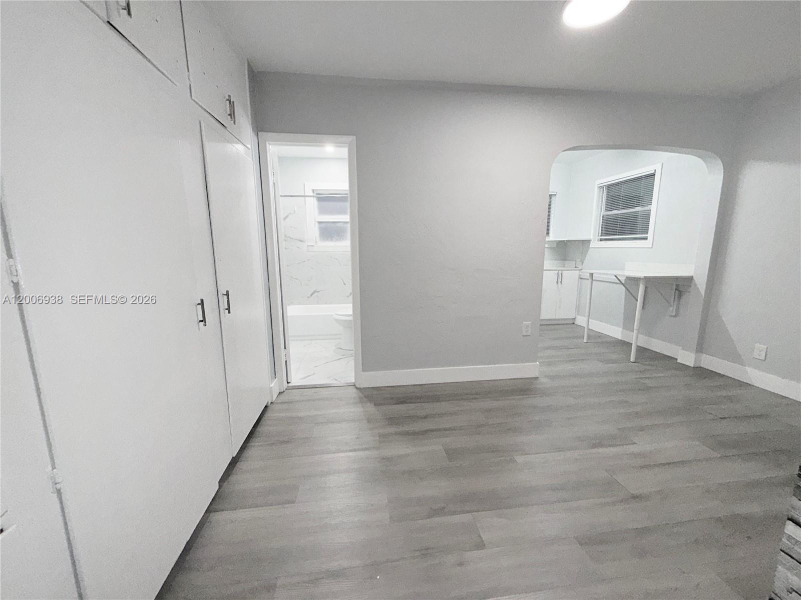 A room with light wood-look flooring, white cabinets, and an arched doorway to a kitchen — 1815 Mckinley St # 1, Hollywood FL 33020, HOLLYWOOD, FL
