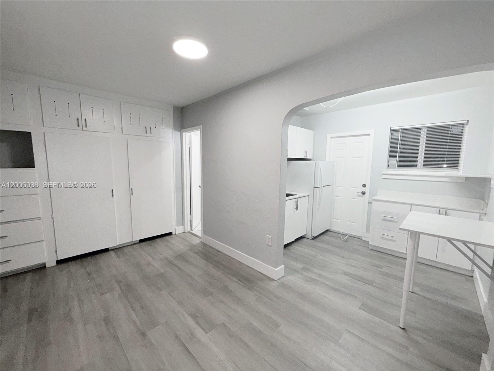 A room with light wood-look flooring features built-in white cabinets and an arched kitchen entryway — 1815 Mckinley St # 1, Hollywood FL 33020, HOLLYWOOD, FL