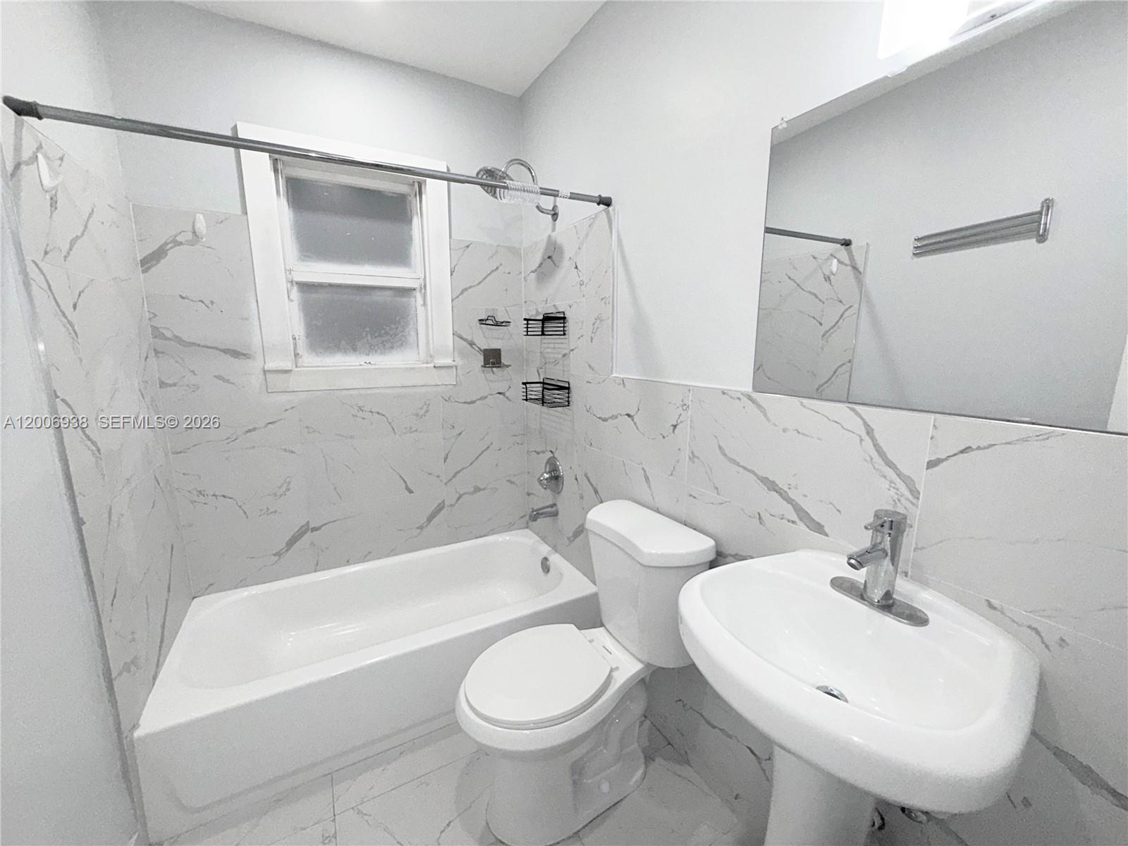 A bathroom features a white pedestal sink, a toilet, and a bathtub with marble-patterned tile — 1815 Mckinley St # 1, Hollywood FL 33020, HOLLYWOOD, FL