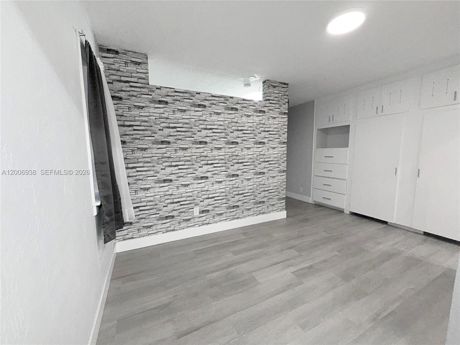 A room with light wood-look flooring, a faux stone accent wall, and built-in white cabinetry — 1815 Mckinley St # 1, Hollywood FL 33020, HOLLYWOOD, FL